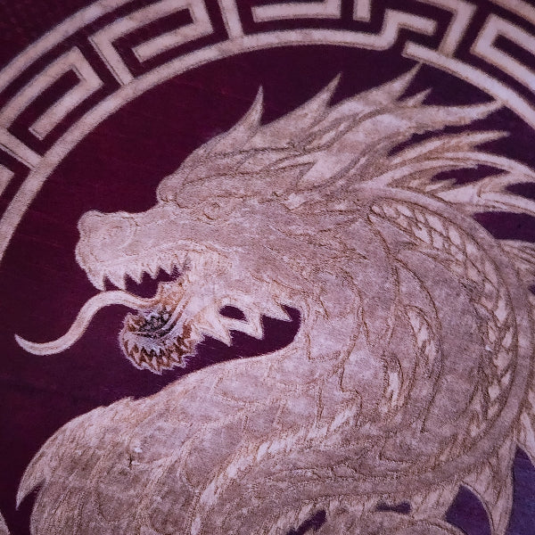 Close-up of a dragon motif in light beige embroidery or print on a deep burgundy background, with a geometric border visible at the top.