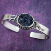 Experience a powerful connection to the wild with this sterling silver cuff - set with a striking organic shaped black druzy and intricately detailed wolves. Showcase your fierce spirit today!