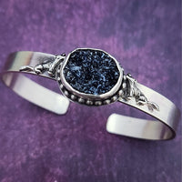 Experience a powerful connection to the wild with this sterling silver cuff - set with a striking organic shaped black druzy and intricately detailed wolves. Showcase your fierce spirit today!