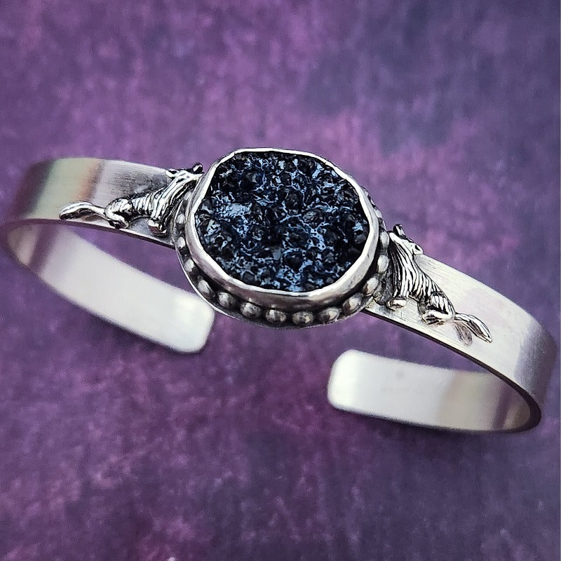 Experience a powerful connection to the wild with this sterling silver cuff - set with a striking organic shaped black druzy and intricately detailed wolves. Showcase your fierce spirit today!