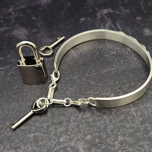 The Cadman Key Keeper Cuff features a chain with a detachable clasp that holds the key to the submissive's lock. With these unique jewelry clasps, the key chain removal is quick and convenient - the key chain can even be linked to a collar during play. Crafted from sterling silver, these luxurious pieces add a sophisticated flair to BDSM boudoirs. By My Secret Heart Studios