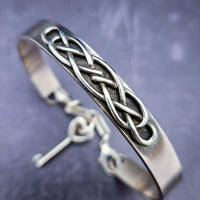 The Cadman Key Keeper Cuff features a chain with a detachable clasp that holds the key to the submissive's lock. With these unique jewelry clasps, the key chain removal is quick and convenient - the key chain can even be linked to a collar during play. Crafted from sterling silver, these luxurious pieces add a sophisticated flair to BDSM boudoirs. By My Secret Heart Studios
