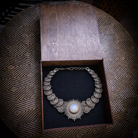 A silver-toned statement necklace with a central sunburst and spiral motifs, displayed inside an open wooden jewelry box on a dark textured surface.