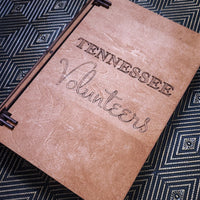 A wooden book box with 'TENNESSEE Volunteers' engraved on the front, shown closed on a black and white geometric patterned surface.