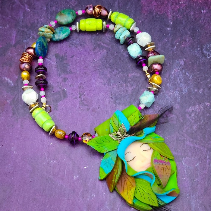 FOREST FAIRY DOLCE is a ONE OF A KIND Artisan Necklace. A sweet little fairy is caught napping in her nest of leaves. Each is a one of a kind piece of wearable art with her own unique look and personality. The faces are hand-painted and then surrounded by hand-cut leaves and collected beads, gemstones and sculpted treasures. 