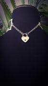 Silver heart-shaped lock on the back of an asymmetrical collar, necklace on a black mannequin with a blurred green background