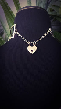 Silver heart-shaped lock on the back of an asymmetrical collar, necklace on a black mannequin with a blurred green background
