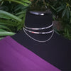 Silver asymmetrical collar with two bands and delicate chain. On a black mannequin with a purple fabric and green leaves in the background