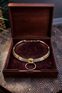Gold necklace with a green stone in a wooden box on a textured surface