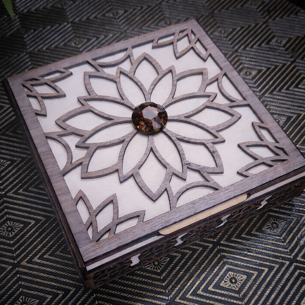 Wooden box with intricate laser-cut design and a central gemstone on a patterned surface.