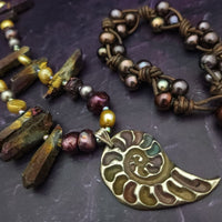Make a bold statement with MARNIA, the one-of-a-kind necklace featuring titanium druzy, freshwater pearls, and a handcrafted bronze medallion ammonite. Turn heads with the vibrant colors and asymmetrical design, guaranteed to make you look and feel unforgettable!
