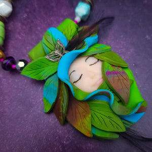 FOREST FAIRY DOLCE is a ONE OF A KIND Artisan Necklace. A sweet little fairy is caught napping in her nest of leaves. Each is a one of a kind piece of wearable art with her own unique look and personality. The faces are hand-painted and then surrounded by hand-cut leaves and collected beads, gemstones and sculpted treasures. 