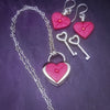 Revamp your locks with a touch of style. This locking soft chain collars features a small heart lock, adorned with a vibrant pink burst pattern and a sparkling center crystal. The embellished lock can also be worn with other collars and chains. Strut your ownership/submission in style ... never wear a plain ole' lock again!!