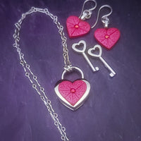 Revamp your locks with a touch of style. This locking soft chain collars features a small heart lock, adorned with a vibrant pink burst pattern and a sparkling center crystal. The embellished lock can also be worn with other collars and chains. Strut your ownership/submission in style ... never wear a plain ole' lock again!!