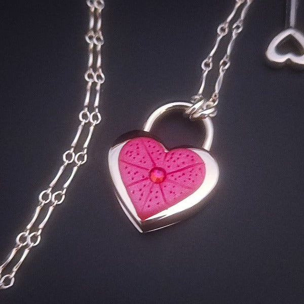 Revamp your locks with a touch of style. This locking soft chain collars features a small heart lock, adorned with a vibrant pink burst pattern and a sparkling center crystal. The embellished lock can also be worn with other collars and chains. Strut your ownership/submission in style ... never wear a plain ole' lock again!!
