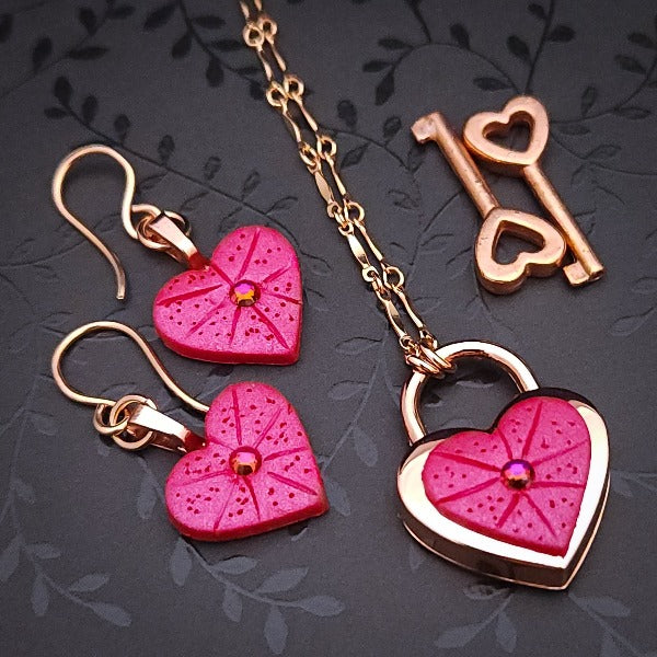 Revamp your locks with a touch of style. This locking soft chain collars features a small heart lock, adorned with a vibrant pink burst pattern and a sparkling center crystal. The embellished lock can also be worn with other collars and chains. Strut your ownership/submission in style ... never wear a plain ole' lock again!!