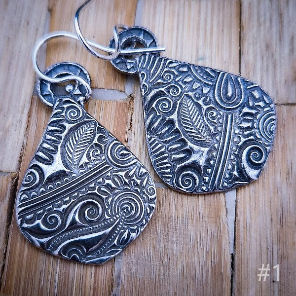 Each pair is created from a lump of cold grey clay that contains microscopic particles of fine silver. Hilly rolls the clay thin, adds a texture, and then meticulously pairs the textures so they are true companion pieces. She even embellishes the back.
