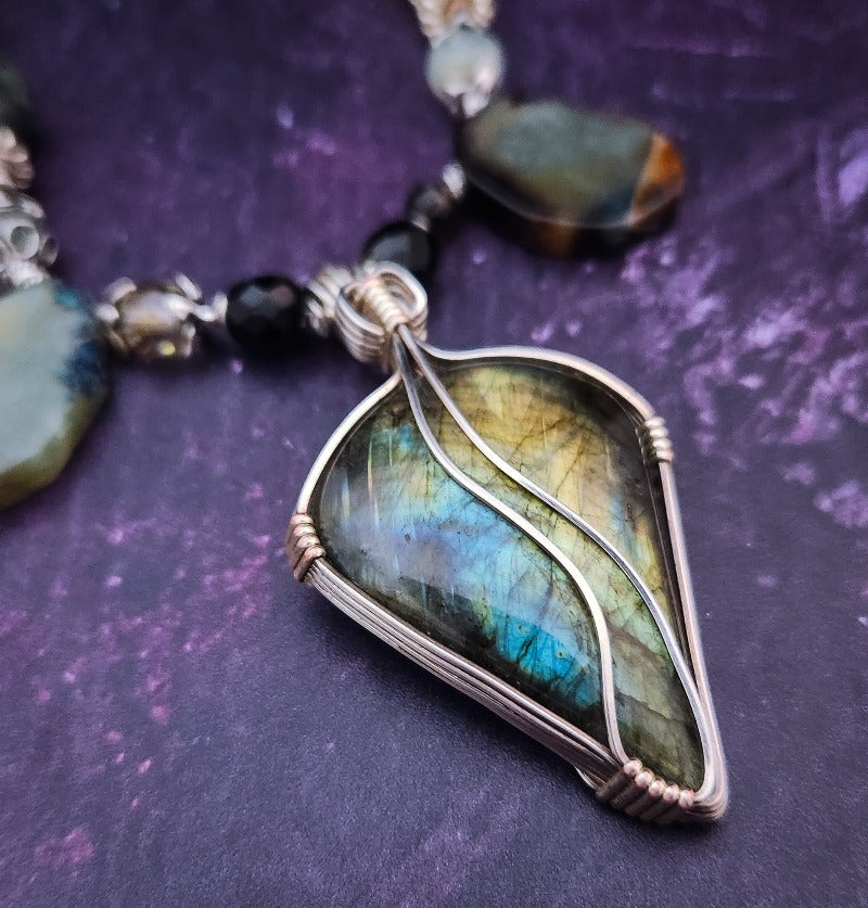We all have a light within, an inner glow that others may see when they connect with our spirit. The shimmer and glow of this Labradorite Cabochon reminds me of this. This asymmetrical collar necklace is a testament to artisan craftsmanship and design. The Labradorite Cabochon is encased in a Wire Wrapped setting with a beautifully fluid look, and sterling silver coiled pieces add a unique look.