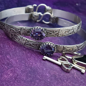 These artisan submissive BDSM handcuff bracelets are hand crafted in a classic floral pattern of sterling silver with faceted Amethyst gemstones.