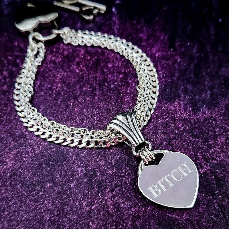 Even a Princess can be a Bitch. A sexy bracelet to celebrate submission. There is a solid HIDDEN O RING behind the heart which can accommodate a leash or be used as a connection point. The PRINCESS SLIDE can be removed and worn on most of our submissive collars, as well as worn on a chain as a pendant. Wear it locked with the small heart lock, or the stainless steel push clasp for discretion. {All included}