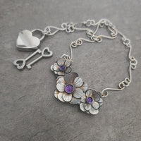 Silver necklace with floral and key charms on a gray background