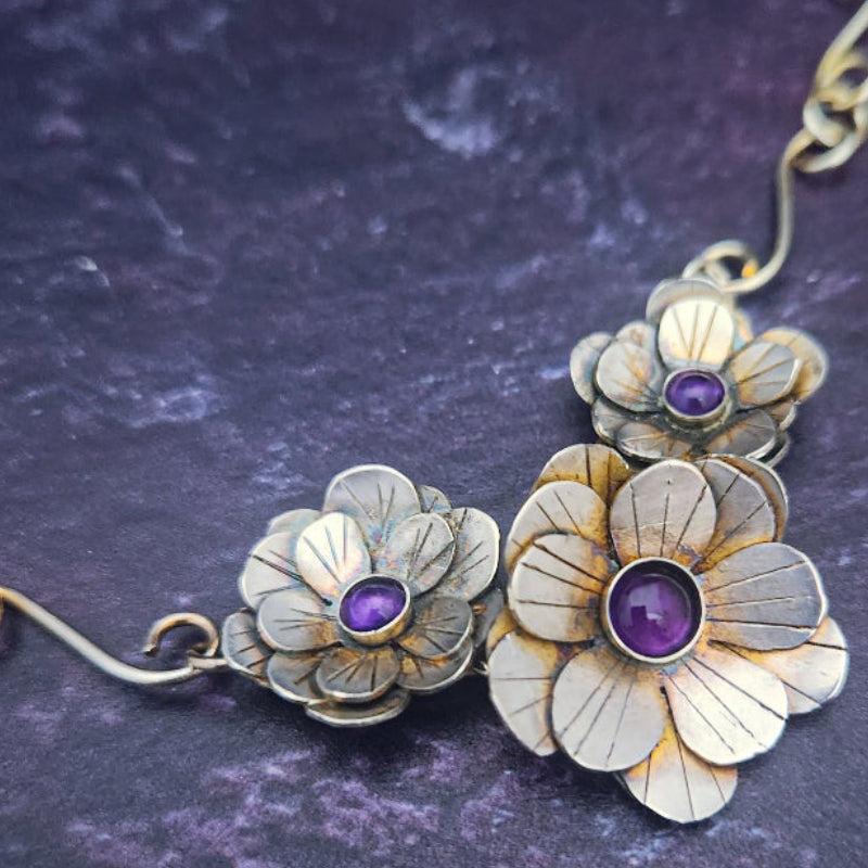 Floral jewelry piece with purple stones on a dark textured background