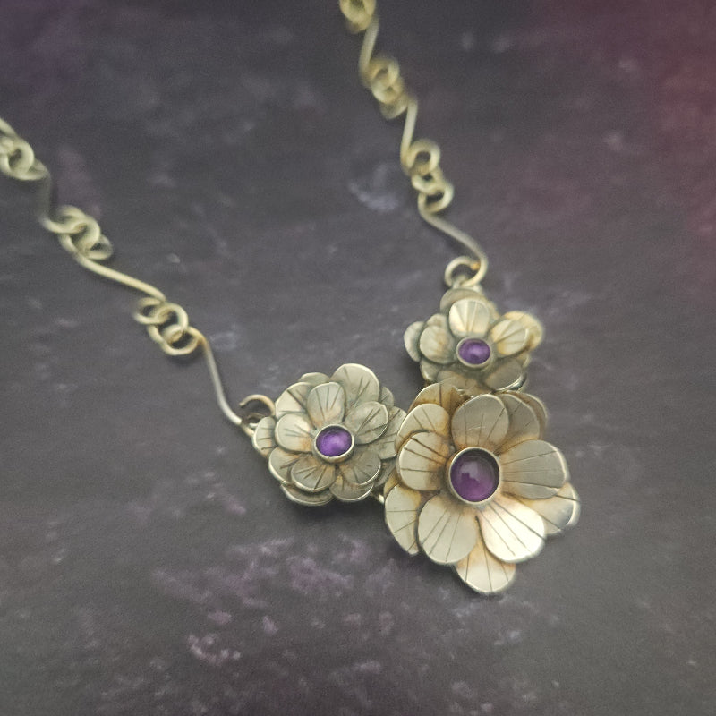 Silver floral necklace with purple stones on a dark background