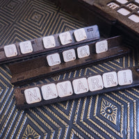 Three wooden Scrabble tiles arranged on a dark textured surface, spelling out 'DEAZB', 'LGO', and 'NAVARRI'.