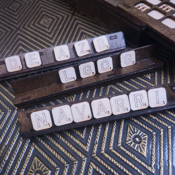Three wooden Scrabble tiles arranged on a dark textured surface, spelling out 'DEAZB', 'LGO', and 'NAVARRI'.