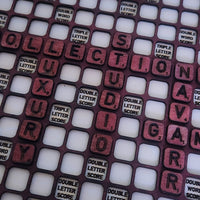 A close-up of a wooden Scrabble-style letter grid with many square tiles in white and reddish-brown wood tones. Some tiles are labeled 'DOUBLE LETTER SCORE' and others are blank or part of the word grid.