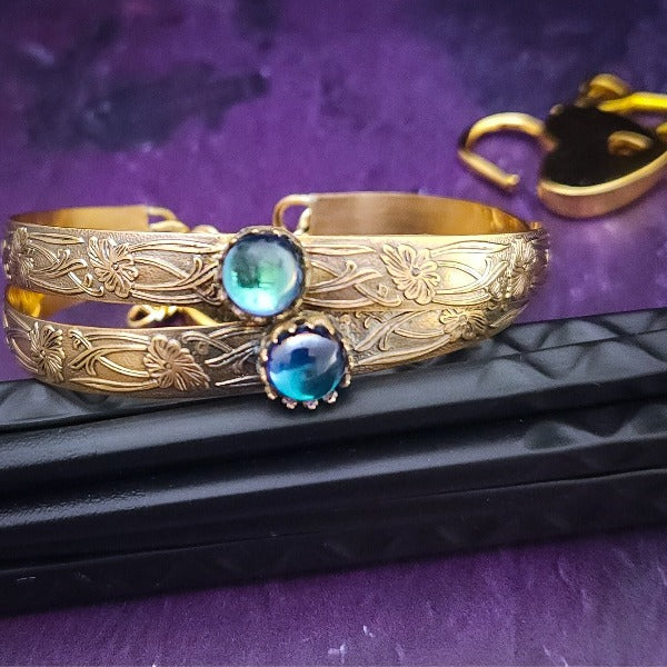 Our NEW GOLD & AZOTIC GALAZIO BLUE TOPAZ Soft and Sweet submissive collar and cuffs are the epitome of feminine grace. Handcrafted with loving care, these artisan-made 14k gold filled submissive collars and cuffs radiate femininity with a floral pattern and a hand-set 8mm Natural Azotic Galazio Blue Topaz. Beautifully feminine and romantic.