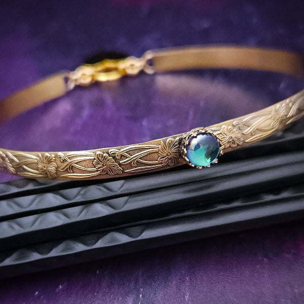 Our Soft and Sweet submissive collar is the epitome of feminine grace. Handcrafted with loving care, this artisan-made 14k gold filled submissive collar radiates femininity with its floral sterling silver pattern and a hand-set 8mm Azotic Galazio Blue Topaz. Beautifully feminine and romantic.