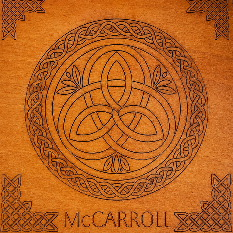 A square wooden plaque or box cover featuring a carved Celtic knot design with a central triquetra-like symbol inside a circular border, corner knot motifs, and the name 'McCARROLL' at the bottom.