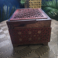 Decorative wooden box with intricate carvings on a textured surface with plants in the background
