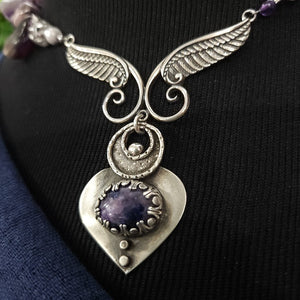 Wear the Velavee Angel Necklace and radiate your inner goddess! Crafted from sterling silver and the rare gemstone Charoite, this one-of-a-kind necklace is adorned with angel wing and a inverted fan shaped medallion, creating a beautiful and unique statement. By My Secret Heart Studios
