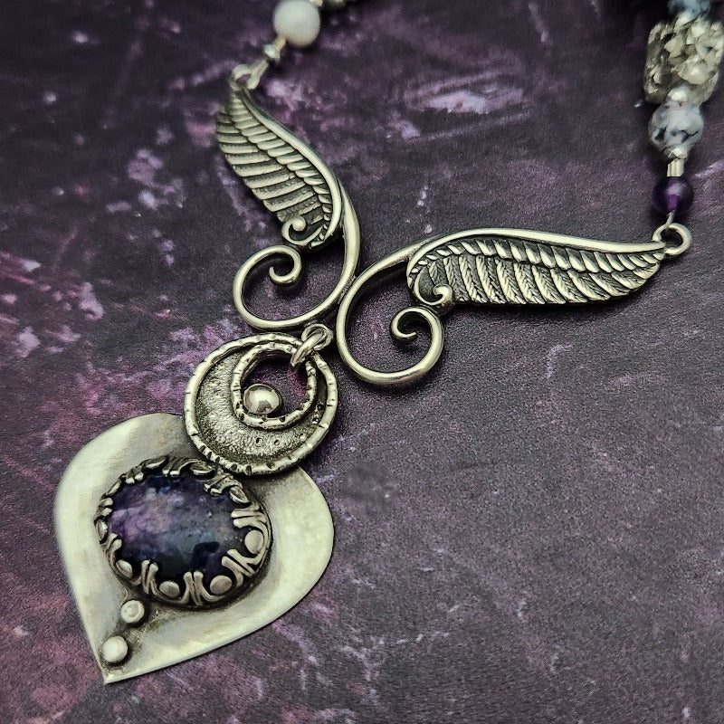 Wear the Velavee Angel Necklace and radiate your inner goddess! Crafted from sterling silver and the rare gemstone Charoite, this one-of-a-kind necklace is adorned with angel wing and a inverted fan shaped medallion, creating a beautiful and unique statement. 