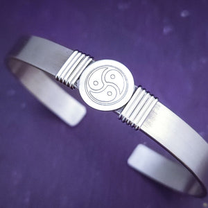 The substantial weight of this sterling cuff lends this a sense of gravitas, while an engraved BDSM symbol is nestled between silver wraps. The simplistic design makes it a perfect companion for almost any other jewelry in your collection. 