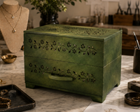 Green jewelry box on a marble surface with tools and jewelry designs in the background