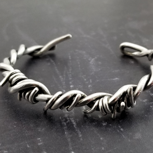 Our version of the a Barbed Wire Cuff, this beast is from our Brambles Collection, inspired by barbs, thorns and prickly things. This cuff is thick, hefty and badass. I create the barbs with comfort in mind, making sure they're smooth and aren't long enough to do real damage, but still just a touch dangerous