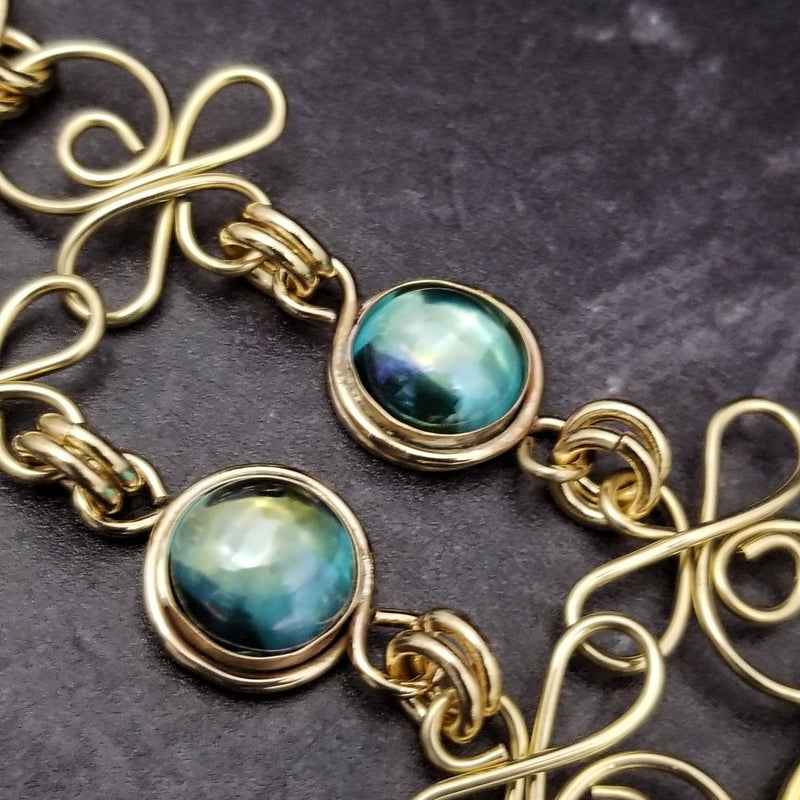 Features chain links inspired by Celtic knots, all created entirely by hand using only a few hand tools. The links are then tumbled with steel shot, creating strength and durability, as well as a silky smoothness.   The center medallion is a gold plated Celtic Triquetra Knot set with natural Rainbow Topaz. By My Secret Heart Studios.