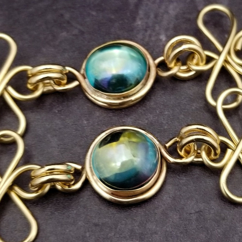 Features chain links inspired by Celtic knots, all created entirely by hand using only a few hand tools. The links are then tumbled with steel shot, creating strength and durability, as well as a silky smoothness.   The center medallion is a gold plated Celtic Triquetra Knot set with natural Rainbow Topaz. By My Secret Heart Studios.