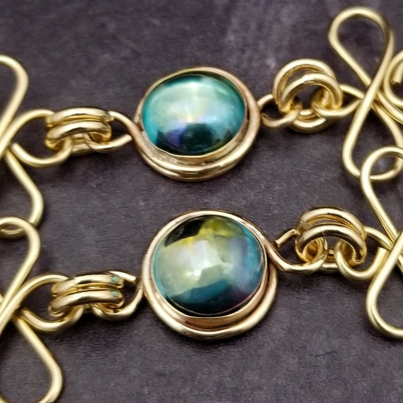 Features chain links inspired by Celtic knots, all created entirely by hand using only a few hand tools. The links are then tumbled with steel shot, creating strength and durability, as well as a silky smoothness.   The center medallion is a gold plated Celtic Triquetra Knot set with natural Rainbow Topaz. By My Secret Heart Studios.