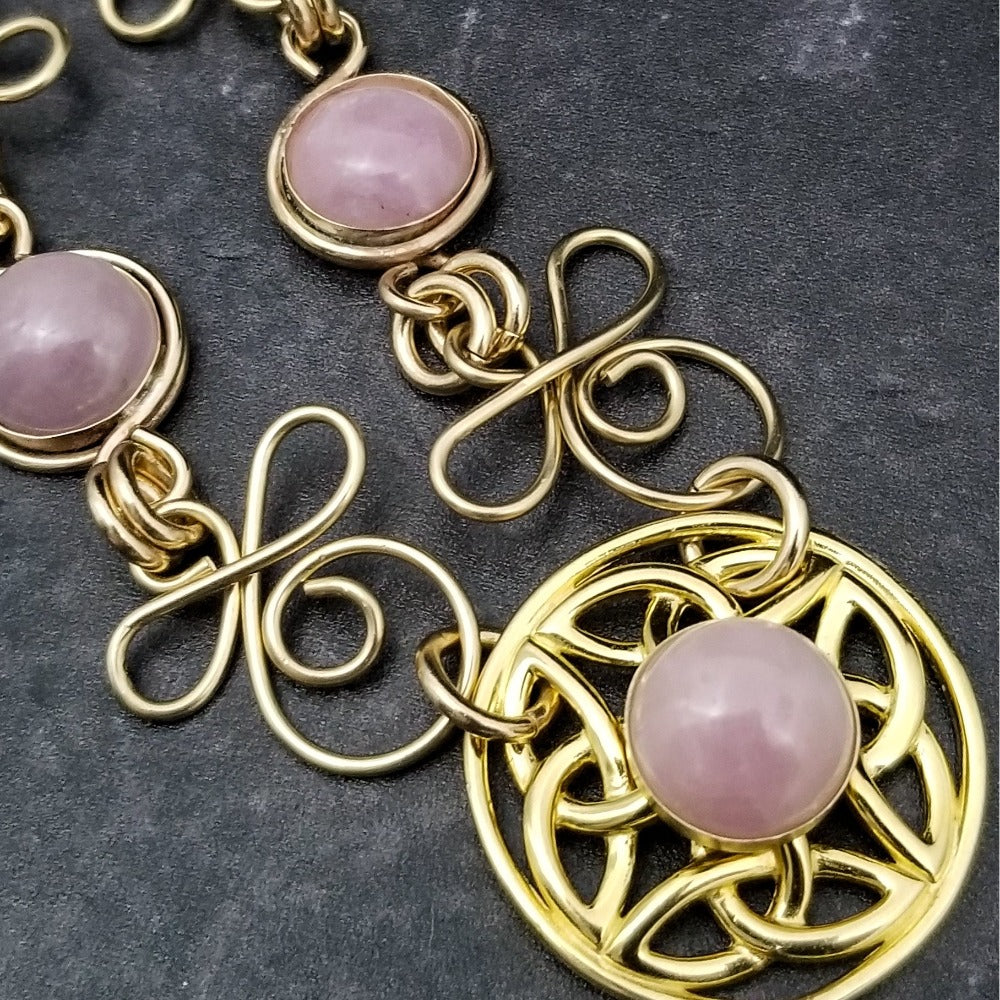 The Celtic Priestess Triquetra Medallion Collar features chain links inspired by Celtic knots, all created entirely by hand using only a few hand tools. The links are then tumbled with steel shot, creating strength and durability, as well as a silky smoothness.   The center medallion is a gold plated Celtic Triquetra Knot set with natural Kunzite. My Secret Heart Studios