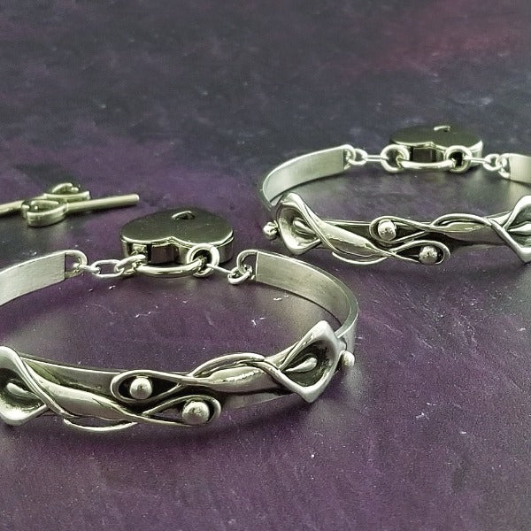 The Calla Lily Handcuff bracelets are a graceful addition to our artisan BDSM jewelry collection. Your submissive is sure to love this feminine and elegant locking cuff. Made in solid sterling silver, with a few links of chain to create a comfortable, 'movable' fit, even when locked. Total discretion!