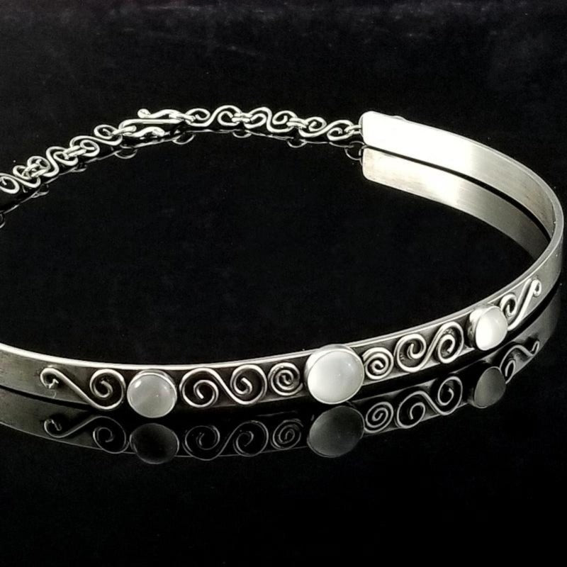 A submissive collar so unique, you'll be proud to wear this collar anywhere! It certainly doesn't 'look' like a BDSM locking collar. You'll treasure this piece! The solid sterling silver collar features White Moonstone cabochons and hand crafted Infinity symbols.