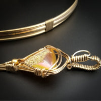 An incredibly luxurious look for a submissive collar. A triangular cut Gold Window Druzy is encased in a gold wire wrapped pendant that can be worn alone or slid onto most of our submissive collars. Featuring stunning open lattice work and a 14k gold filled chain that can be worn with a traditional clasp, or locked with a lock and key.