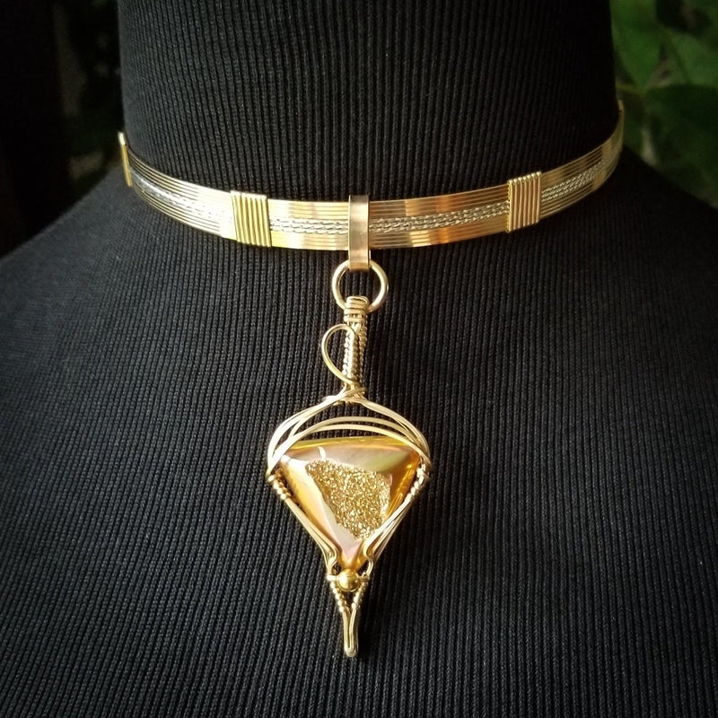 An incredibly luxurious look for a submissive collar. A triangular cut Gold Window Druzy is encased in a gold wire wrapped pendant that can be worn alone or slid onto most of our submissive collars. Featuring stunning open lattice work and a 14k gold filled chain that can be worn with a traditional clasp, or locked with a lock and key.