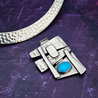 Add some personality to your collar. This collar slide is handcrafted in sterling silver with a bezel set Turquoise cabochon. A very Asian inspired asymmetrical design. The pendant comes with a sterling silver chain, but the unique clip design allows you to also clip the pendant over your own beaded necklaces for a dramatic and unique style.