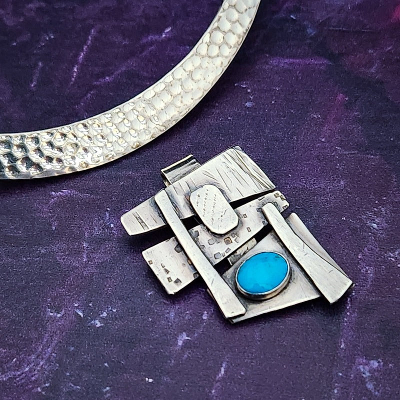 Add some personality to your collar. This collar slide is handcrafted in sterling silver with a bezel set Turquoise cabochon. A very Asian inspired asymmetrical design. The pendant comes with a sterling silver chain, but the unique clip design allows you to also clip the pendant over your own beaded necklaces for a dramatic and unique style.