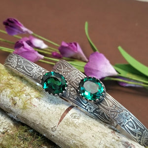 These artisan BDSM submissive handcuff bracelets are hand crafted in a classic floral pattern of sterling silver with faceted emerald gemstones.